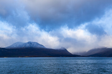 Autumn landscape of the Lyngen Alps in Northern Norway with snowy peaks, dramatic clouds, and a tranquil fjord.