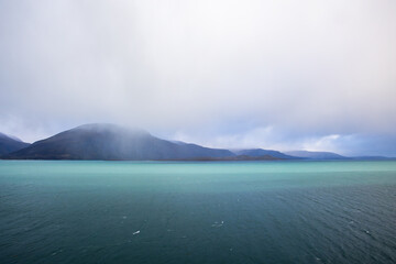 Autumn landscape of the Lyngen Alps in Northern Norway with snowy peaks, dramatic clouds, and a tranquil fjord.