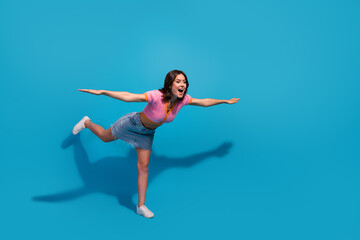 Obraz premium Young woman joyfully posing against vibrant blue background in dynamic playful stance, wearing trendy pink and blue casual outfit