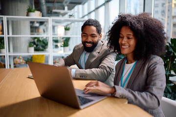 Happy black coworkers using laptop while working in office.