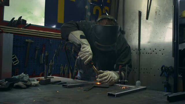 MIG welder, wearing welding personal protective equipment and clothing, working in a workshop, medium shot. Service, industry, and fabrication concepts
