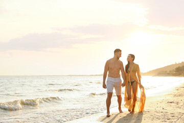 Happy young couple walking together on beach at sunset