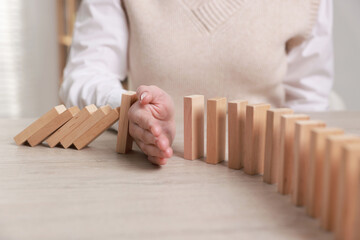 Woman stopping wooden blocks from falling at table, closeup. Domino effect