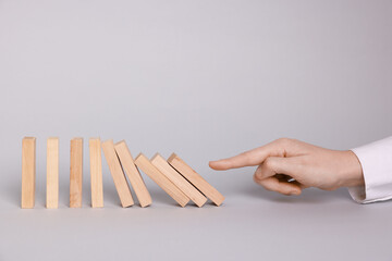 Domino effect. Woman pushing wooden blocks on light background, closeup