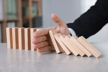 Man stopping wooden blocks from falling at table, closeup. Domino effect