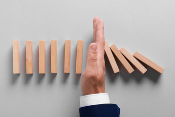 Man stopping wooden blocks from falling on grey background, top view. Domino effect