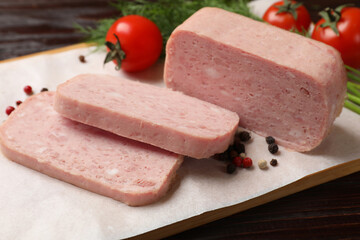Pieces of tasty canned meat and peppercorns on wooden table, closeup
