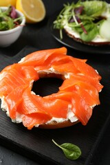 Delicious bagels with salmon and vegetables on black table, selective focus