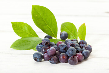 Heap of blueberries and their leaves on white wooden background