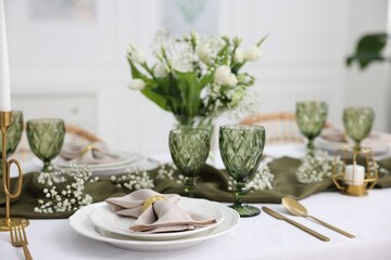Color accent table setting with glasses, flowers and green napkins indoors, closeup
