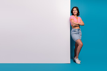 Stylish young woman standing confidently before a vibrant blue backdrop wearing casual denim and a pink top