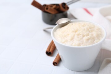 Tasty rice pudding with cinnamon served on white tiled table, closeup. Space for text