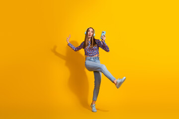 Girl Expressing Joy with Smartphone on Vibrant Yellow Backdrop for Advertising