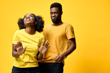Happy African American couple dancing in bright yellow clothing against a vibrant yellow...