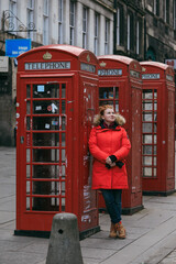 Tourist wearing a red coat exploring historic telephone booths in Scotland on a chilly day