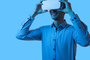 A businessman in a blue shirt interacting with virtual reality using VR goggles, smiling and...