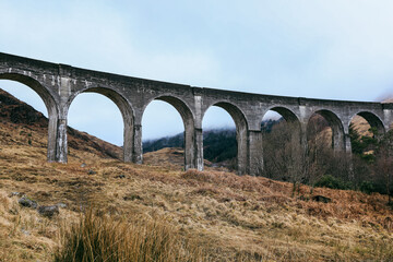 Fototapeta premium Glenfinnan Viaduct stands majestically against a rugged Scottish landscape on a cloudy day
