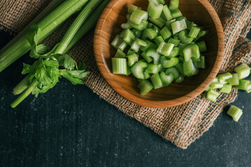 Fresh celery stalks and chopped pieces in a wooden bowl on a rustic dark table. Organic green...