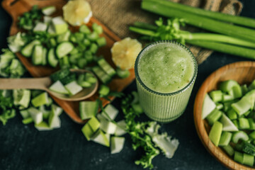 Fresh green smoothie in a textured glass surrounded by chopped ingredients including cucumber,...