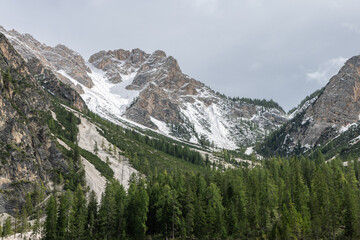 Croda del Becco mountain range surround Lake Braies, with steep cliffs, snow-covered ridges, and dense evergreen forests creating a dramatic alpine scene in the Dolomites, Italy