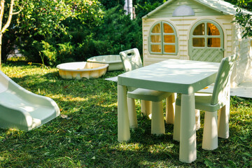 Children's backyard play area with a plastic slide, sandbox, table, chairs, and a small playhouse...