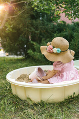 Toddler in a straw hat with floral accents playing with pastel sandbox toys on the lawn. Perfect...