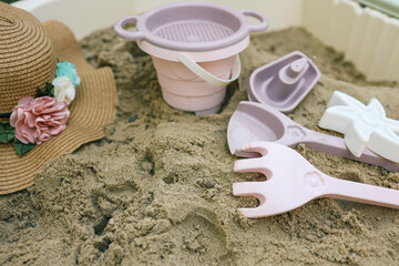 Plastic sandbox toys, including a bucket, sieve, rake, and boat, arranged in a backyard sandbox....