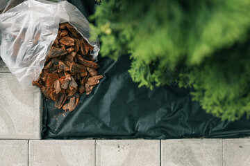 Bag of decorative bark mulch on black landscaping fabric near paving stones and green bushes. Used...