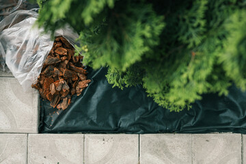 Bag of decorative bark mulch on black landscaping fabric near paving stones and green bushes. Used...