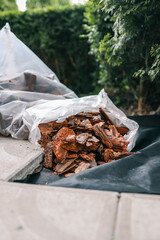 Bag of decorative bark mulch on black landscaping fabric near paving stones and green bushes. Used for soil protection, moisture retention, and weed control in garden landscaping