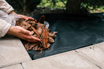 Hands pouring decorative bark mulch onto a black landscape fabric for garden bed protection....