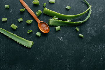 Fresh aloe vera gel in a wooden spoon with cut aloe leaves on a dark textured surface. Natural...