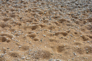 A detailed close-up shot of a beach with a mix of sand and pebbles, showcasing the natural texture and pattern of the shoreline.