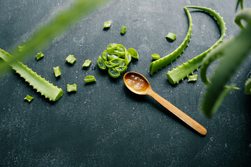 Fresh aloe vera gel in a wooden spoon with cut aloe leaves on a dark textured surface. Natural...