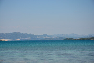 Peljesac Bridge spans the calm, turquoise waters of the Adriatic Sea, connecting the mainland to the Peljesac peninsula, as seen from the shore of Peljesac