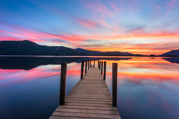 Romantic sunset over wooden jetty with reflections on a summer evening in The Lake District, UK.