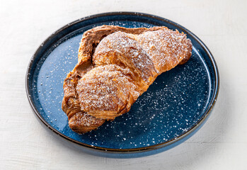 Sweet Italian croissant filled with caramel cream on blue ceramic plate isolated on white table