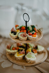 A beautifully arranged two-tier wooden serving tray filled with an assortment of colorful canapés, featuring fresh vegetables, salami, olives, cheese, and cream spread on whole grain bread
