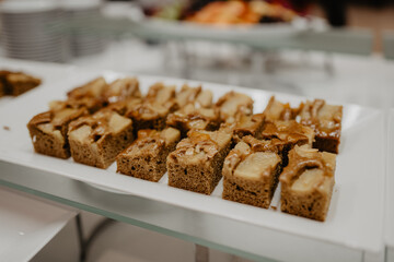 A close-up of a white rectangular serving platter filled with freshly baked caramelized apple cake cut into small square pieces, featuring a golden brown sponge base topped 