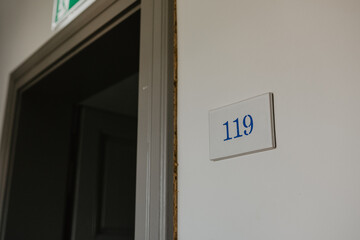 Open door leading to a dimly lit room with a white wall featuring a blue-numbered room sign 
