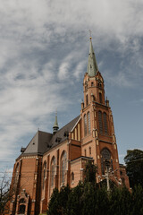 Majestic Gothic-style red brick church with towering spires, arched stained glass windows, and intricate architectural details set against a dramatic sky