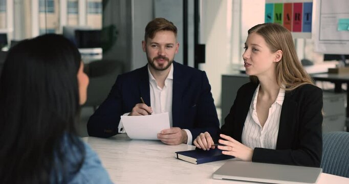 HR managers team interviewing job candidate at meeting table. Couple of businesspeople talking to female colleague, employee, coworker, business partners sitting opposite