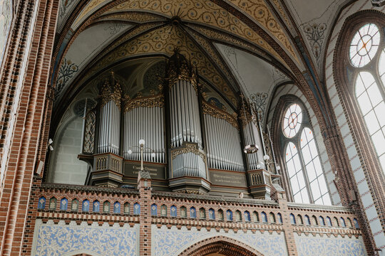A grand pipe organ with intricate gold detailing set against the stunning vaulted ceiling and stained glass windows of a historic Gothic church interior