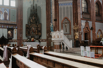 A beautifully decorated interior of a historic Catholic church featuring intricate brickwork, ornate stained glass windows, wooden pews
