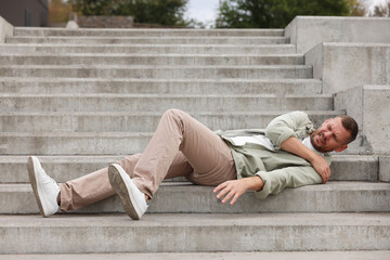 Man with injured arm on stairs outdoors after fall. Dangerous accident