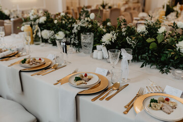 An elegantly decorated banquet table set for a formal event with luxurious gold-rimmed plates, fine dining silverware, crystal glassware, and gourmet plated meals