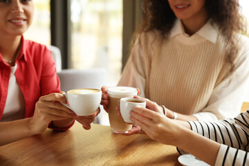 Women with cups of delicious coffee drinks at wooden table in cafe, closeup