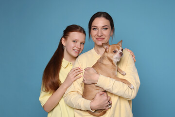 Portrait of beautiful mother with teenage daughter and cute Chihuahua dog on light blue background