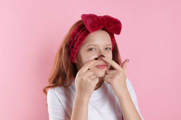 Teenage girl popping pimple on her face against pink background. Acne problem