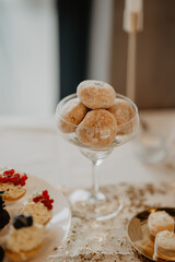 A close-up of a beautifully arranged dessert table featuring a glass coupe filled with sugar-dusted mini doughnuts, surrounded by elegant pastries and confections, creating a luxurious 
